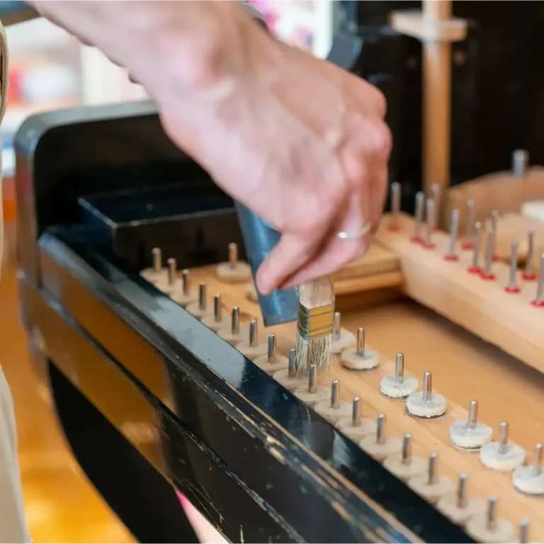 Offenes Klavier mit herausgenommenen Tasten. Klaviaturboden wird mit Pinsel und Staubsauger im Zuge einer Klavierreinigung gereinigt.